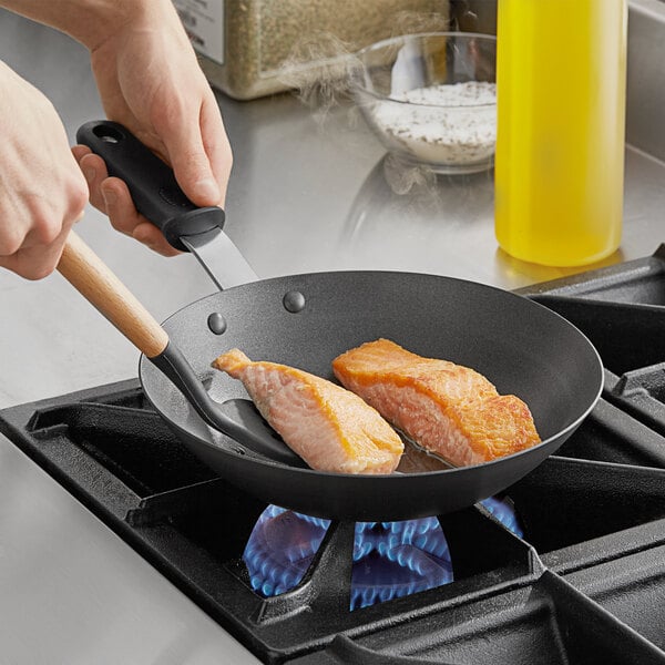 A person using a Vollrath carbon steel non-stick fry pan to cook salmon.