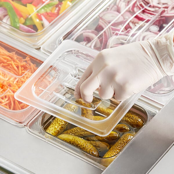 A gloved hand using a Choice clear polycarbonate food pan lid to cover a plastic tray of food.