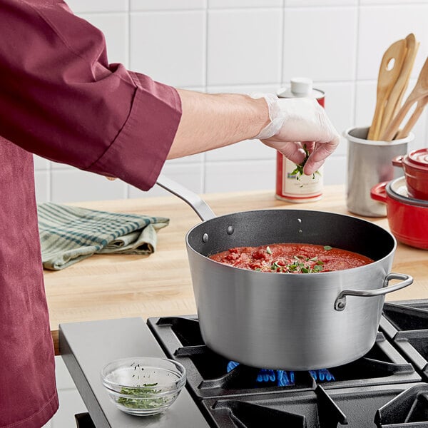 Chef sprinkling basil into a pasta sauce simmering in a non-stick saucepan