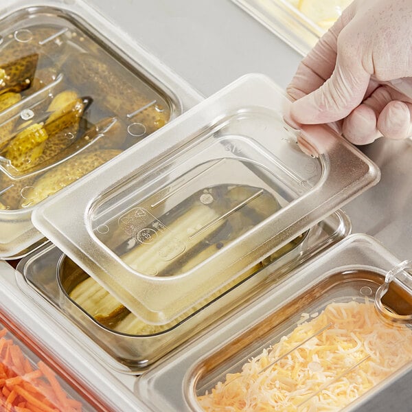 A person putting food in a clear plastic food container with a clear polycarbonate lid.