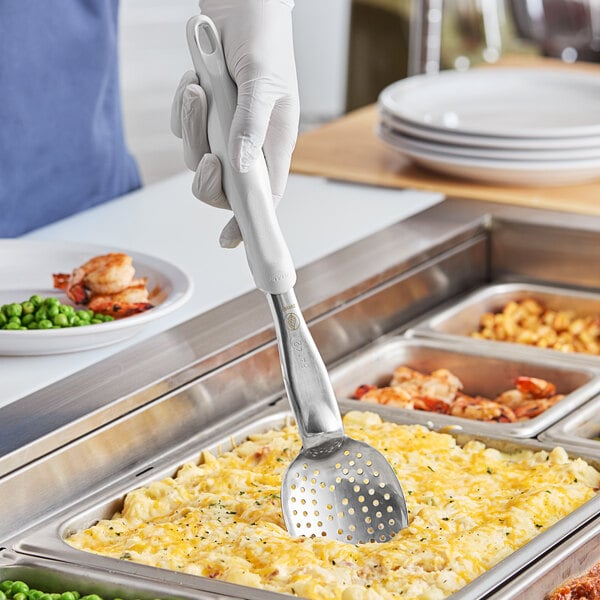 A hand holding a Vollrath Jacob's Pride perforated basting spoon over food.