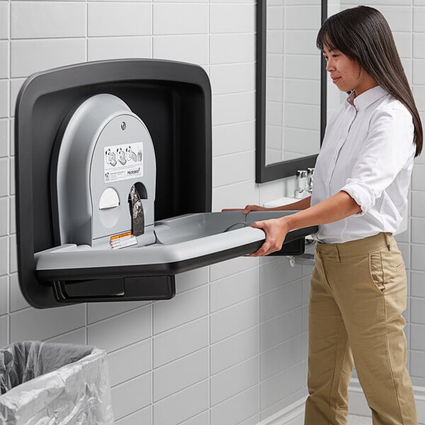 A woman using a Koala Kare stainless steel baby changing station.