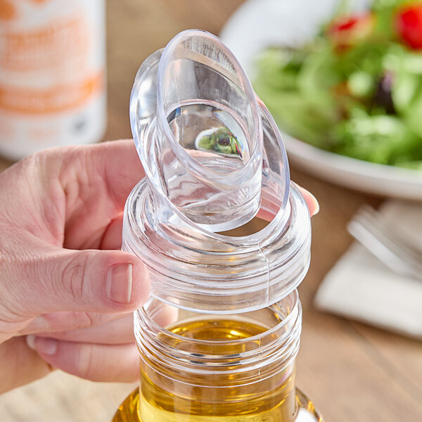 A hand using a Cal-Mil no-drip pour lid to pour olive oil into a bottle on a table.