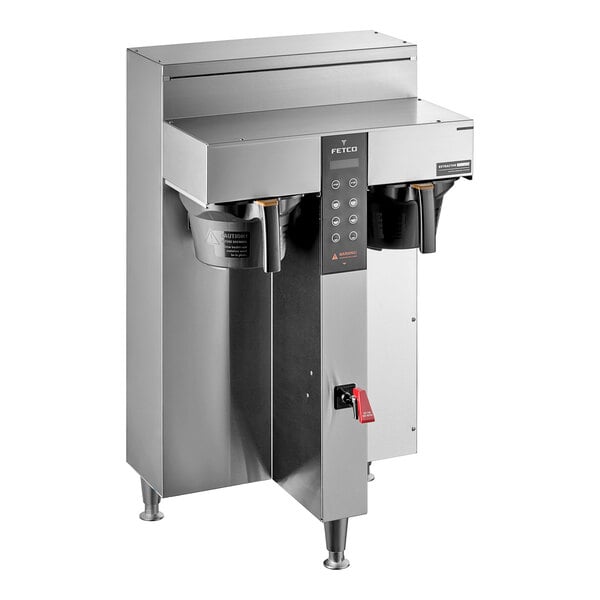 A silver stainless steel Fetco CBS-1252 Plus Series Twin automatic coffee brewer on a counter with black and red buttons.