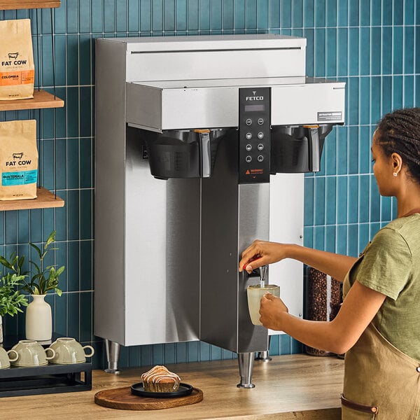 A woman pouring water into a Fetco CBS-1252 coffee machine.