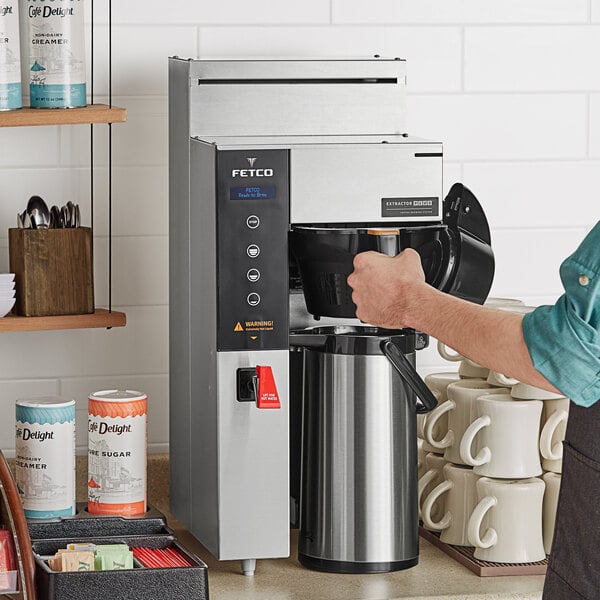 A person using a Fetco CBS-1231 coffee machine to pour coffee into a white mug.