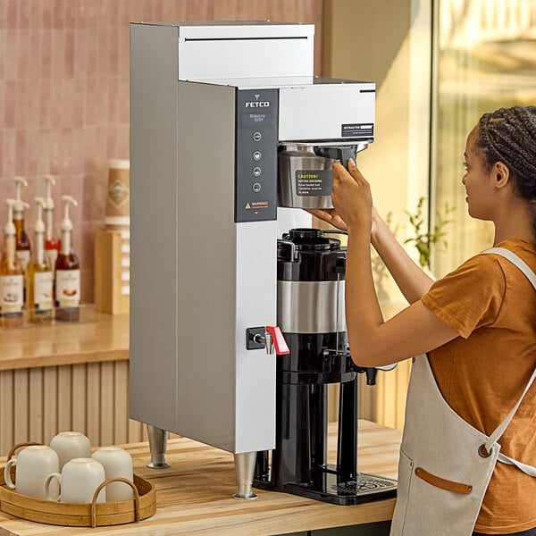 A woman using a Fetco CBS-1251 Plus Series automatic coffee machine on a counter in a coffee shop.