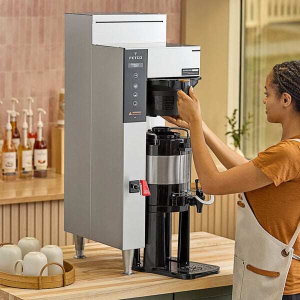 A person using a Fetco CBS-1251 Plus automatic coffee machine in a coffee shop.
