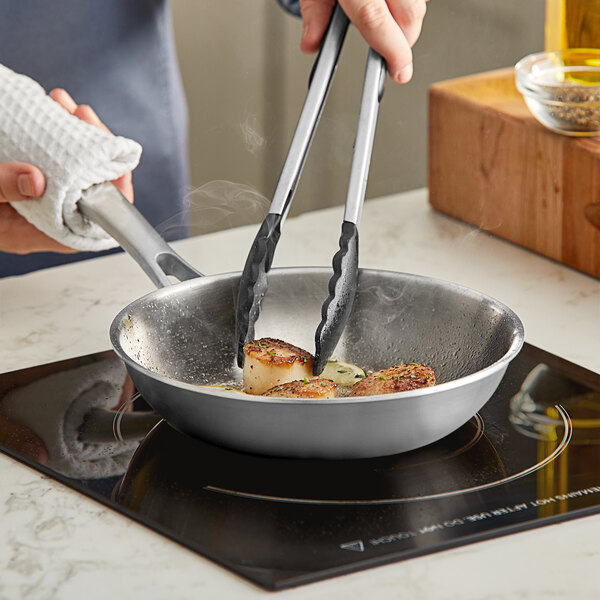 A person cooking food in a Vigor stainless steel fry pan.