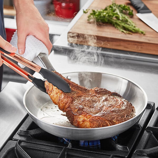 A person cooking a steak in a Vigor stainless steel fry pan.
