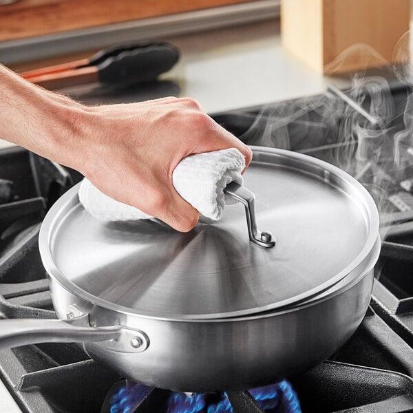 A hand using a towel to clean a Vigor SS3 Series stainless steel pot lid.