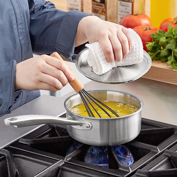 A woman stirring a Vigor stainless steel sauce pan on a stove.