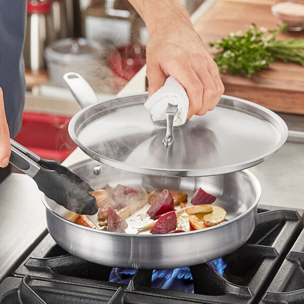 A person cooking food in a Vigor stainless steel saute pan on a stove.