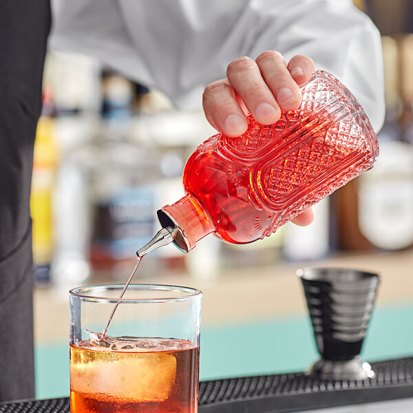 A bartender pouring Barfly bitters into a glass on a counter.