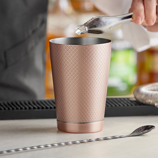 A person using a Barfly antique copper cocktail shaker to pour a drink.