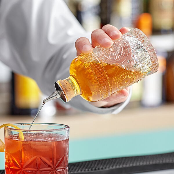 A hand pouring liquid from a Barfly Retro Design Glass Bitters Bottle into a drink.