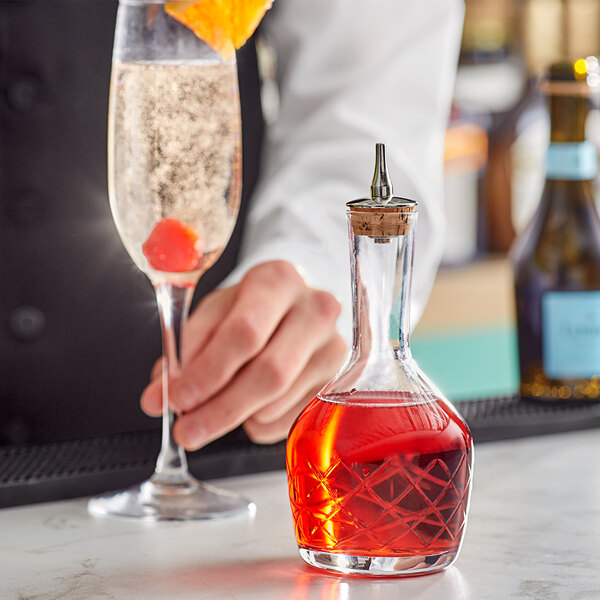A person holding a Barfly glass flask with red liquid over a table in a cocktail bar.