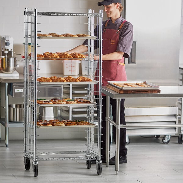 A woman in a chef's uniform standing next to a Regency side load sheet pan rack filled with doughnuts.