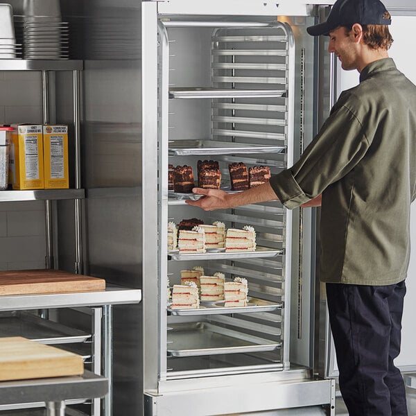 A man taking a tray of cakes from a Regency end load sheet pan rack in a refrigerator.