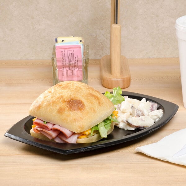 Ham sandwich on a ciabatta roll with potato salad on a black foam platter