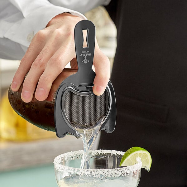 A person using a Barfly black spring bar strainer to pour a drink.