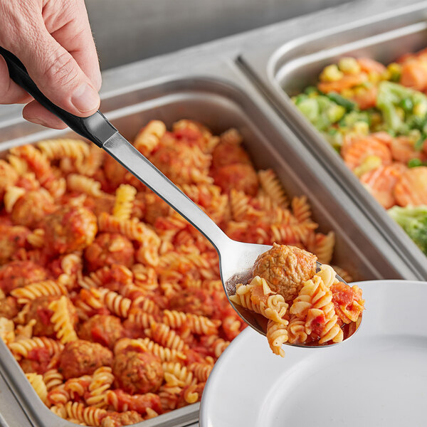 A person using a Vollrath stainless steel spoon with a black Kool-Touch handle to serve pasta.