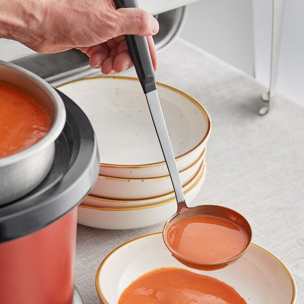 A person using a Vollrath stainless steel ladle to pour soup into a bowl.