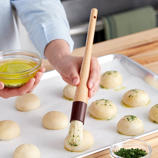 A person using a Vollrath round boar bristle pastry brush with a wooden handle to brush dough.