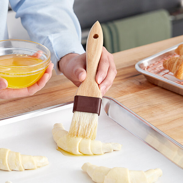 A person using a Vollrath Boar Bristle Pastry Brush to baste a croissant.