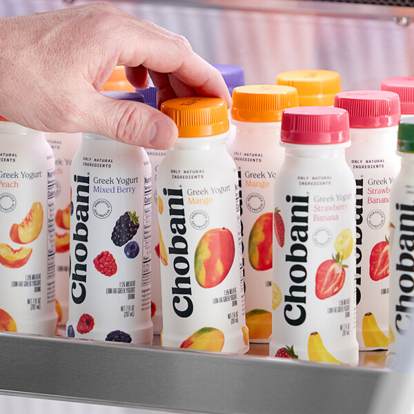 A hand holding a Chobani Low-Fat Mango Greek Yogurt Drink bottle with a yellow cap.