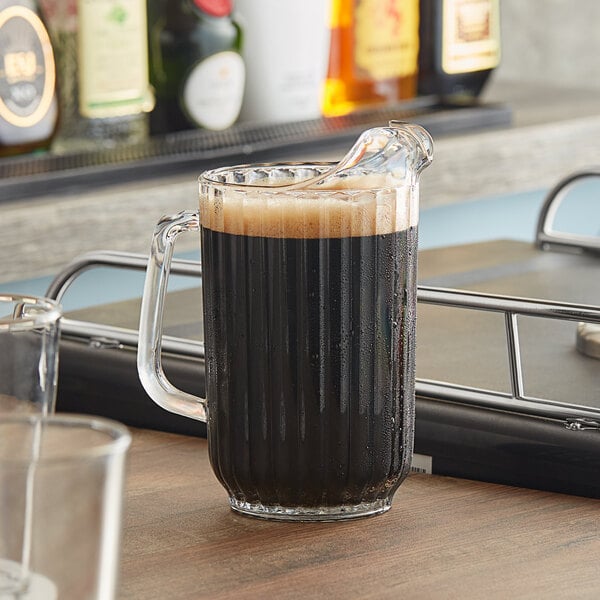 A Cambro clear plastic pitcher filled with brown liquid on a table.