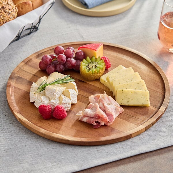 A round acacia wood serving board displaying assorted cheeses, meats, and fruits.