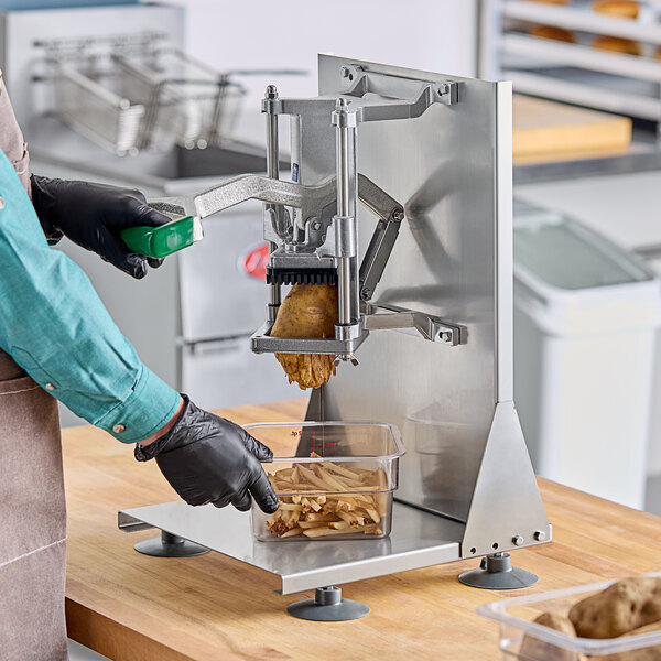 A person in a blue shirt and black gloves uses a Garde heavy-duty French fry cutter on a countertop.