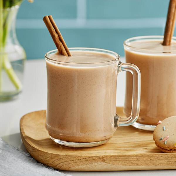 A glass of Dona Masala Chai with cinnamon sticks on a wooden tray.