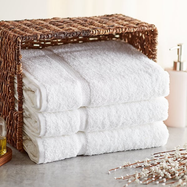 A stack of Lavex Premium white bath towels in a basket.