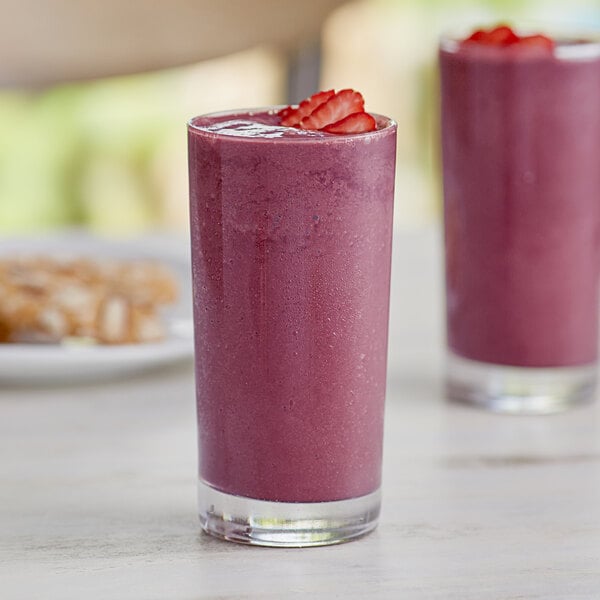 Two glasses of pink smoothie with strawberries on top on a table.