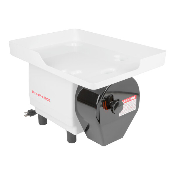 A white and black electric device with a rectangular tray on top, supported by four legs and featuring a power cord and a warning label on the front.