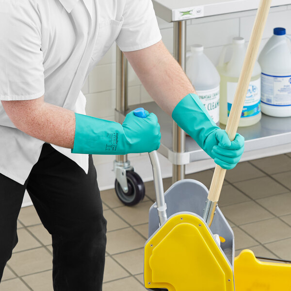 A person wearing green Ansell AlphaTec gloves and holding a mop.