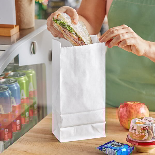 A person putting a sandwich in a white paper bag.