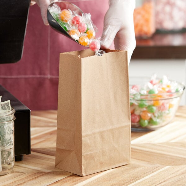 A person in gloves pouring candy into a ChoiceHD Natural Kraft bag on a wood surface.