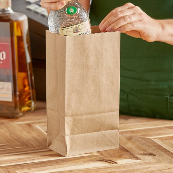 A hand putting a bottle of alcohol into a ChoiceHD natural Kraft paper bag.