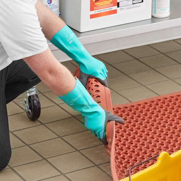 A person wearing green and gray Ansell rubber gloves using a plastic container.