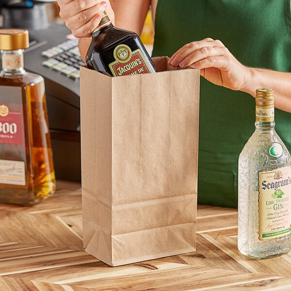 A woman putting a bottle of liquor into a ChoiceHD natural kraft bag.