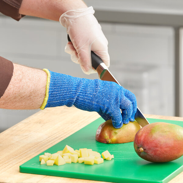 A person wearing blue Ansell knitted gloves peeling a mango.