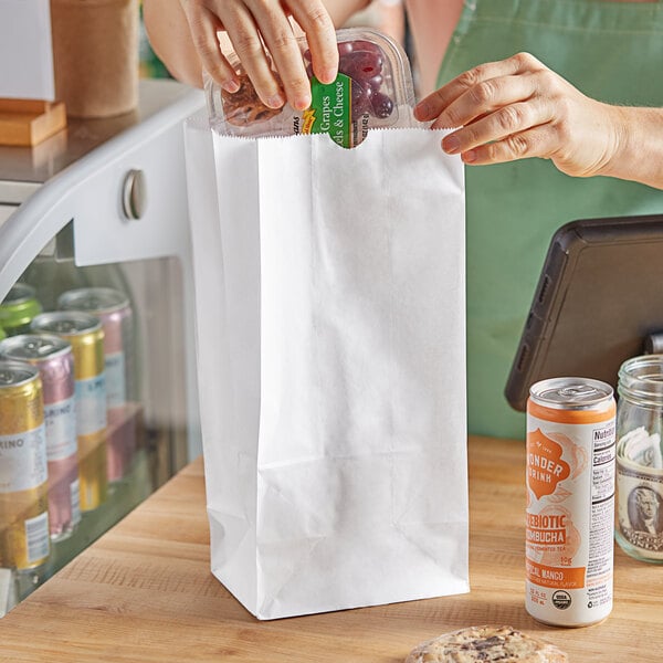 A woman putting food in a Choice white paper bag on a table.