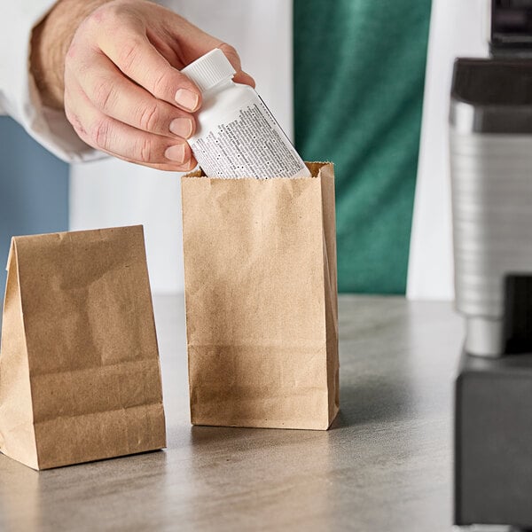 A person putting a white bottle into a natural brown Kraft paper bag on a counter.