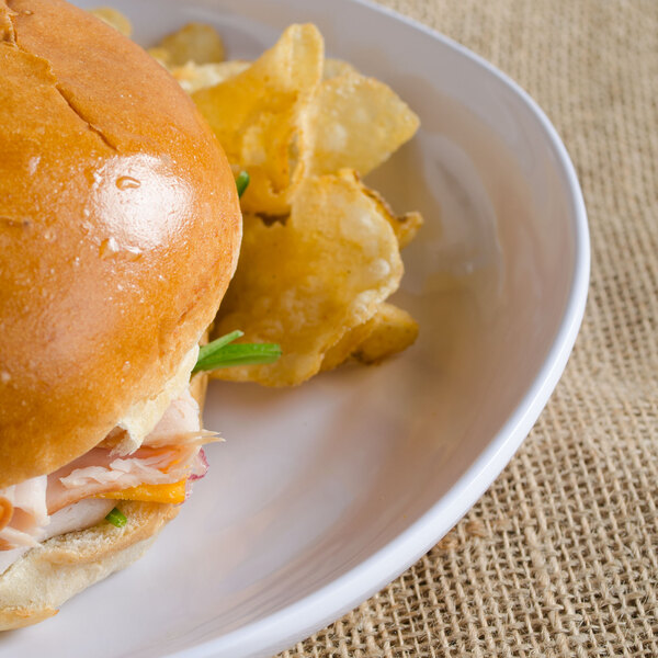 A sandwich and potato chips on a Carlisle white square melamine plate.