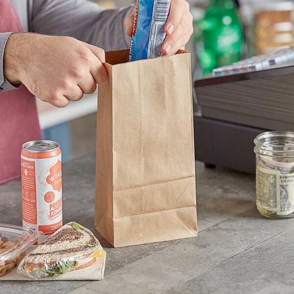 A person opening a ChoiceHD brown paper bag with a handle to put food inside.