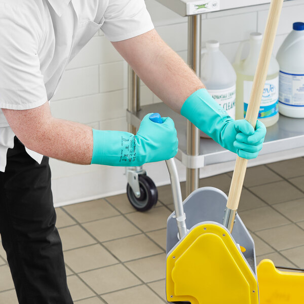 A person wearing green Ansell AlphaTec Solvex gloves and using a mop to clean a floor.