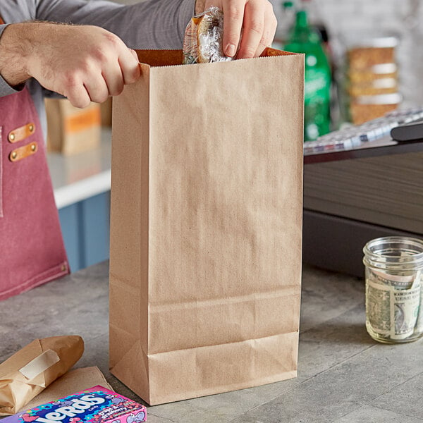 A person holding a brown ChoiceHD paper bag with a handle full of food.